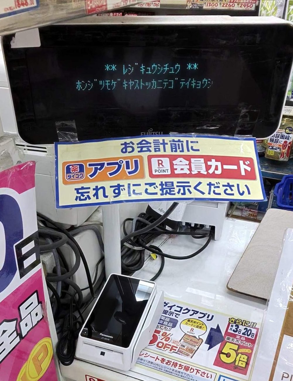 ダイコクドラッグのレジ。会計前にアプリか会員カードを見せるよう案内する札と、カードの読み取り機