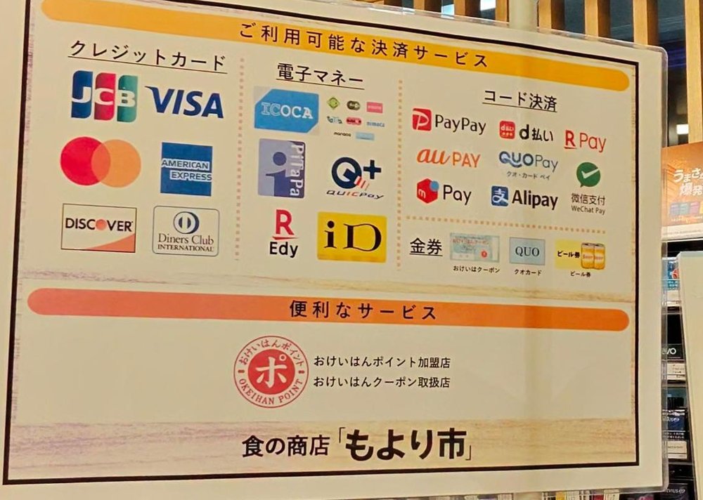 もより市のレジにある「ご利用可能な決済サービス」の案内。クレジットカード（JCB・VISA・Mastercard・American Express・Discover・Diners Club）、電子マネー（ICOCAなどの交通系IC・PiTaPa・QUICPay・楽天Edy・iD）、コード決済（PayPay・d払い・楽天ペイ・au PAY・QUOカードPay・WeChat Pay・メルペイ・Alipay）、金券（おけいはんクーポン・QUOカード・ビール券）、おけいはんポイント加盟店