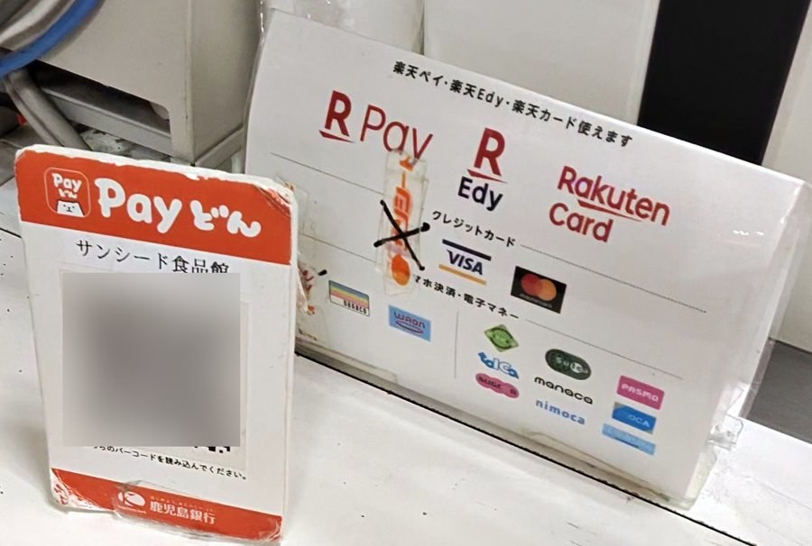 レジに置かれた鹿児島銀行「Payどん」のQRコードの台と、楽天ペイ・楽天Edy・楽天カードの古い案内